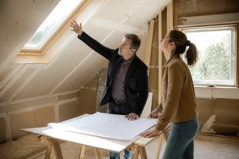Architekt und Hausbesitzer besprechen die Planung eines neuen Dachfensters, um Größe und Position optimal für den Raum festzulegen.