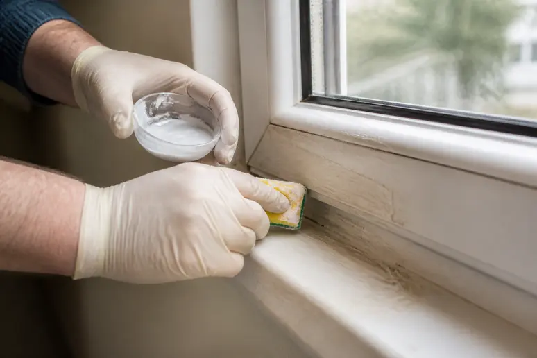 Ein Mann trägt Natronpaste auf einen vergilbten weißen Kunststofffensterrahmen auf, um ihn zu reinigen.