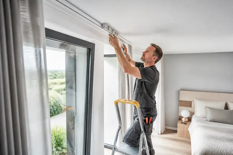 Handwerker installiert Gardinenschiene für Gardinen im Schlafzimmer