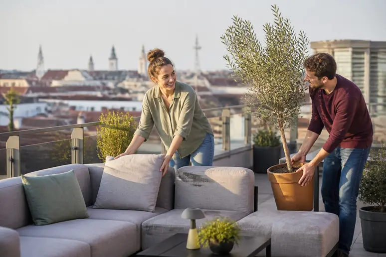 Junge Paare arrangieren Möbel und Pflanzen für die gestaltung einer Dachterrasse, stilvolle Atmosphäre über den Dächern