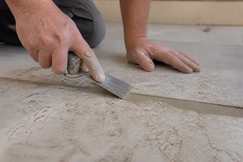 Hand glättet mit Spachtelmasse eine tiefe Fuge zwischen strukturierten Fliesen für eine ebene Oberfläche.