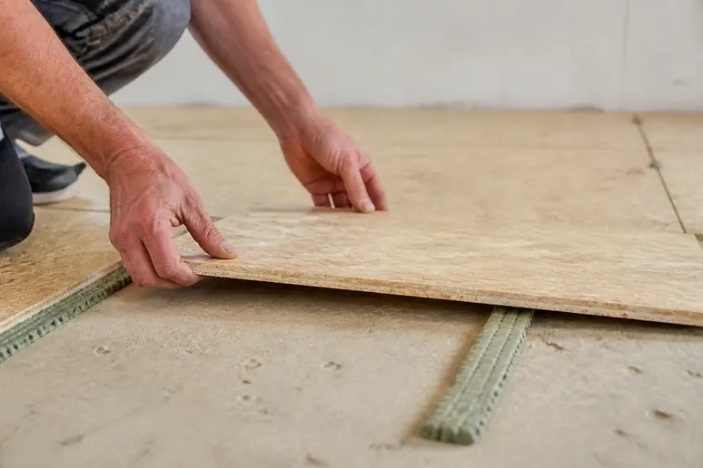 Hände legen OSB-Platten und Nivellierstreifen auf unebenen Untergrund, um Unebenheiten auszugleichen.