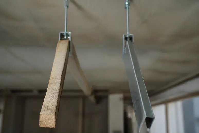 Verzogene Holzlatte neben geradem Metallprofil im Vergleich für Deckenunterkonstruktionen.
