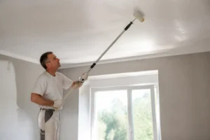 Decke streichen tipps: Mann streicht sorgfältig Decke Richtung Fenster für streifenfreie Ergebnisse.