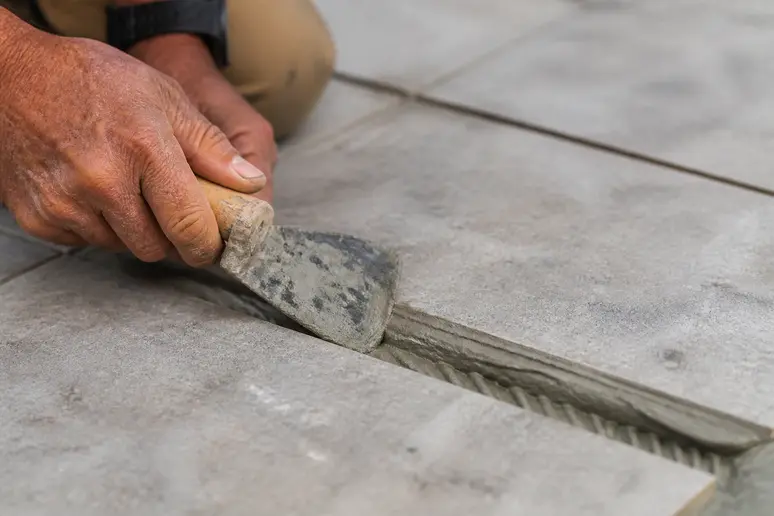 Hände eines Handwerkers tragen präzise Fliesenkleber in eine vorbereitete Fuge auf.
