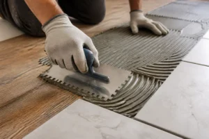 Handwerker klebt Fliesen auf Holz: Sorgfältige Verlegung von Keramikfliesen auf Holzboden vermeidet Risse. Naheinstellung des Klebeprozesses.
