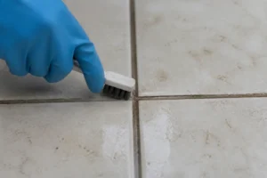 Hand reinigt schmutzige Fliesenfugen mit einer Bürste, zeigt saubere Fugen nach der Reinigung.