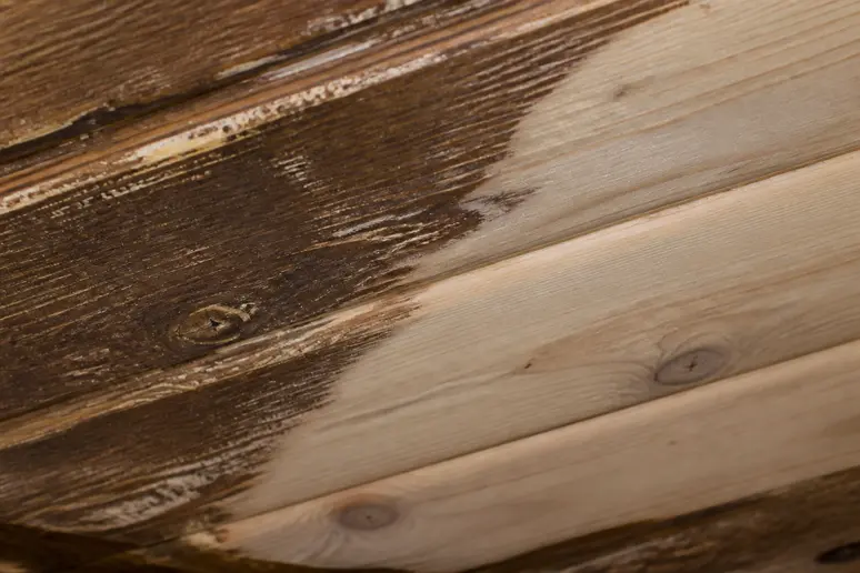 Untere rechte Ecke einer Holzdecke, grob und fleckig, kontrastiert mit dem glatt geschliffenen Bereich darüber.