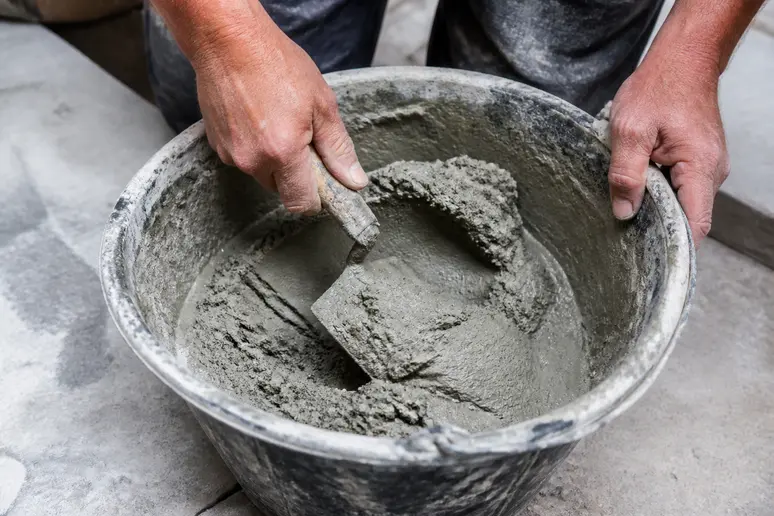 Hände mischen Mörtel in rundem Kübel mit Stuckateurspachtel für Wandreparaturen.