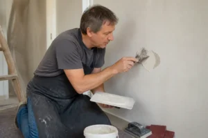 Mann füllt Löcher in der Wand mit Spachtelmasse, Detailansicht des Heimwerkerprojekts zur Wandreparatur.