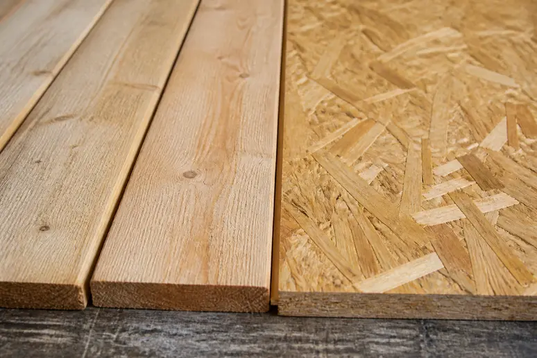 Nahaufnahme von Rauhspund-Holzbrettern mit sichtbarer Maserung und einer glatten OSB-Platte nebeneinander auf einer Werkbank.