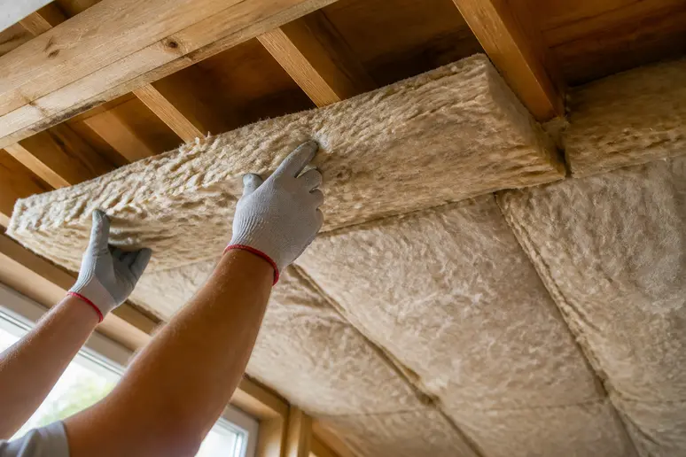 Handwerker verlegt zwei versetzt und überlappende Lagen Dämmmaterial auf einer Holzbalkendecke.