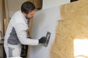 Handwerker spachtelt OSB Platten präzise für glatte Oberflächen, beugt Rissen und Aufquellen vor.