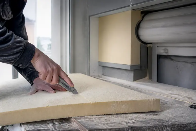 Hand schneidet präzise biegsame Dämmplatte für Rollladenkasten zu.