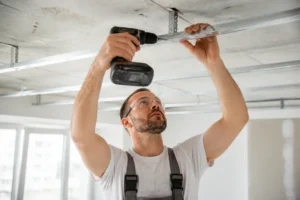 Handwerker hängt Trockenbaudecke ab und montiert Abhänger für die Deckenkonstruktion.