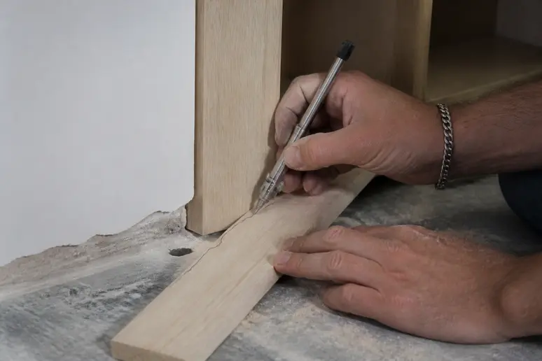 Handwerker überträgt unebene Wandkonturen mit einem Zirkel auf eine Passleiste für den Einbauschrank.