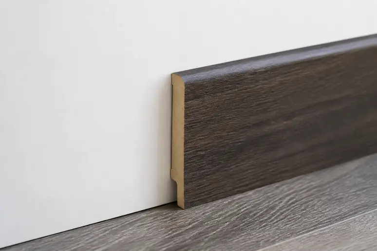 Weiße MDF Sockelleiste mit folierter Holzoptik an einer geraden Wand montiert