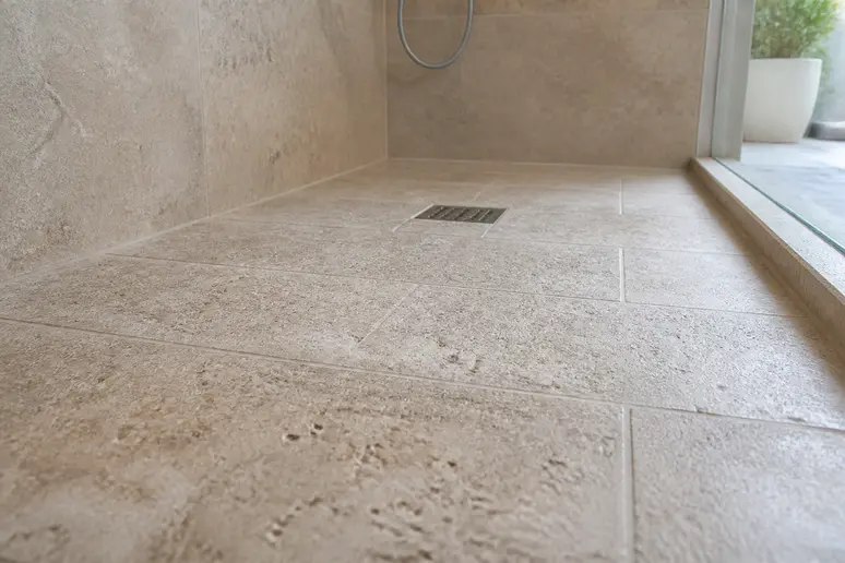 Gezierte Travertinfliesen auf einem barrierefreien Duschboden mit rutschhemmender Oberflächenstruktur.
