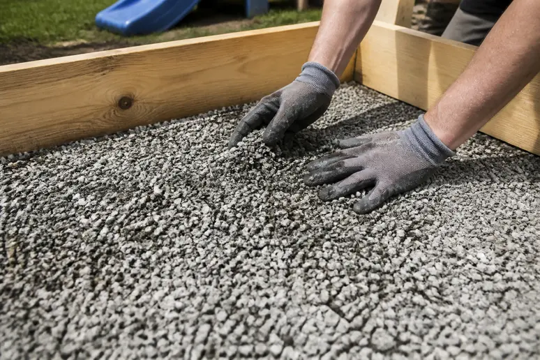 Hände verteilen Kies als Drainage im Holtrahmen für einen Sandkasten