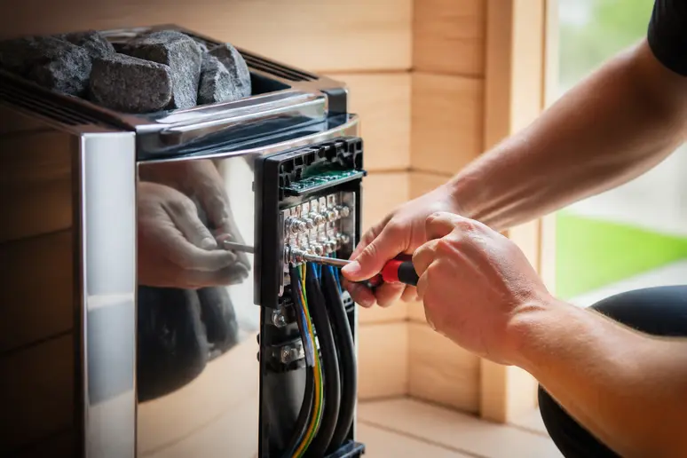 Elektriker schließt das Starkstromkabel an die Steuerung eines Elektro-Saunaofens an